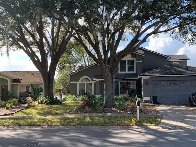 Two mature oaks shading the front yard of a gray two-story home